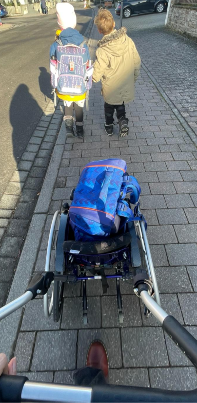 Eine Gruppe ist mit Schulranzen und Rollstuhl auf einem Gehweg unterwegs.