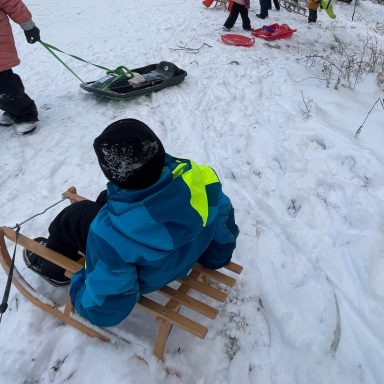 Ein Kind sitzt auf einem Holzschlitten im Schnee.