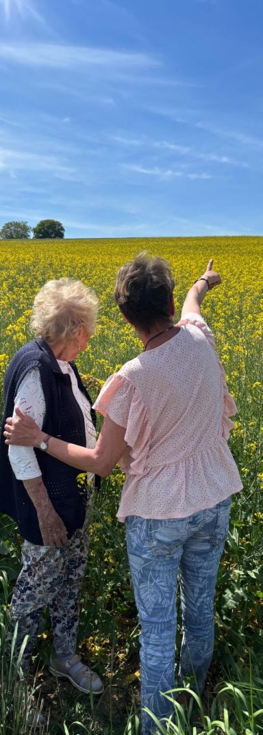 Zwei Frauen gehen gemeinsam an einem blühenden Feld spazieren.