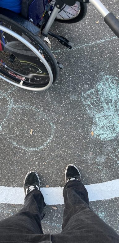 Kreidezeichnungen auf dem Boden neben einem Rollstuhl.